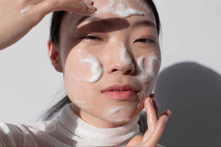 A woman with foam cleanser on their face gently massaging their skin.